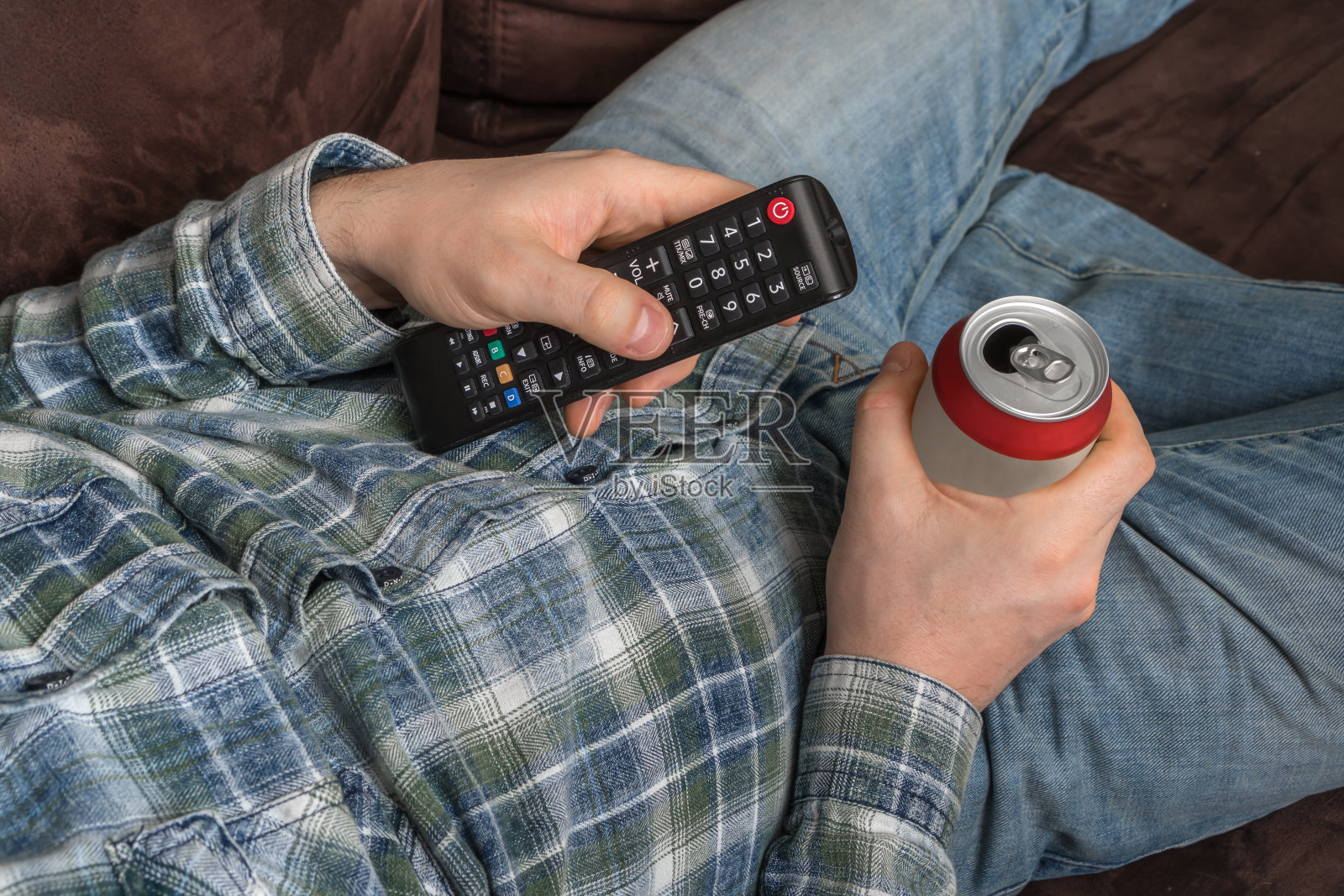 那家伙躺在沙发上，拿着电视遥控器，喝着啤酒照片摄影图片