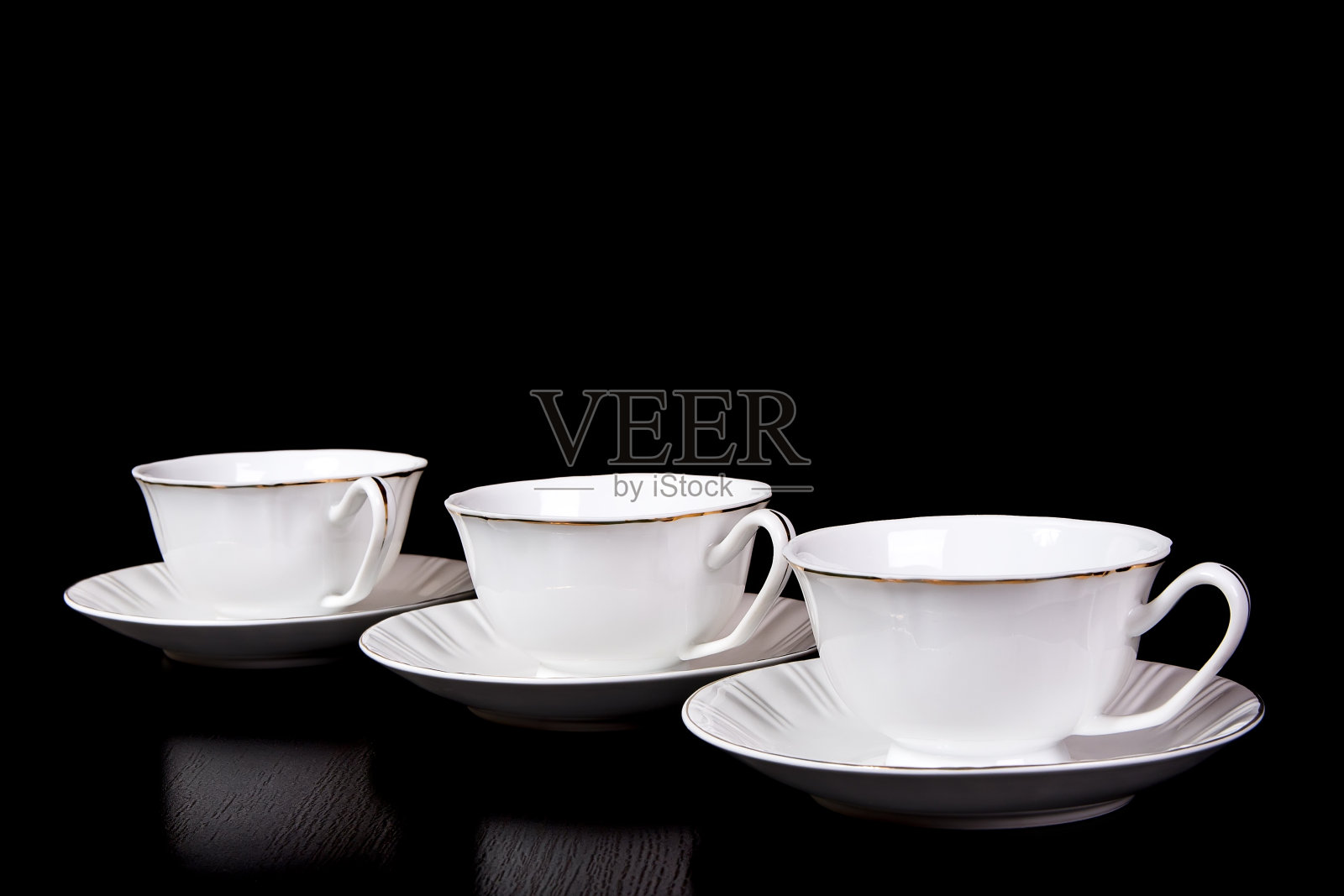 黑底的桌子上放着三个白色的茶杯和茶托照片摄影图片
