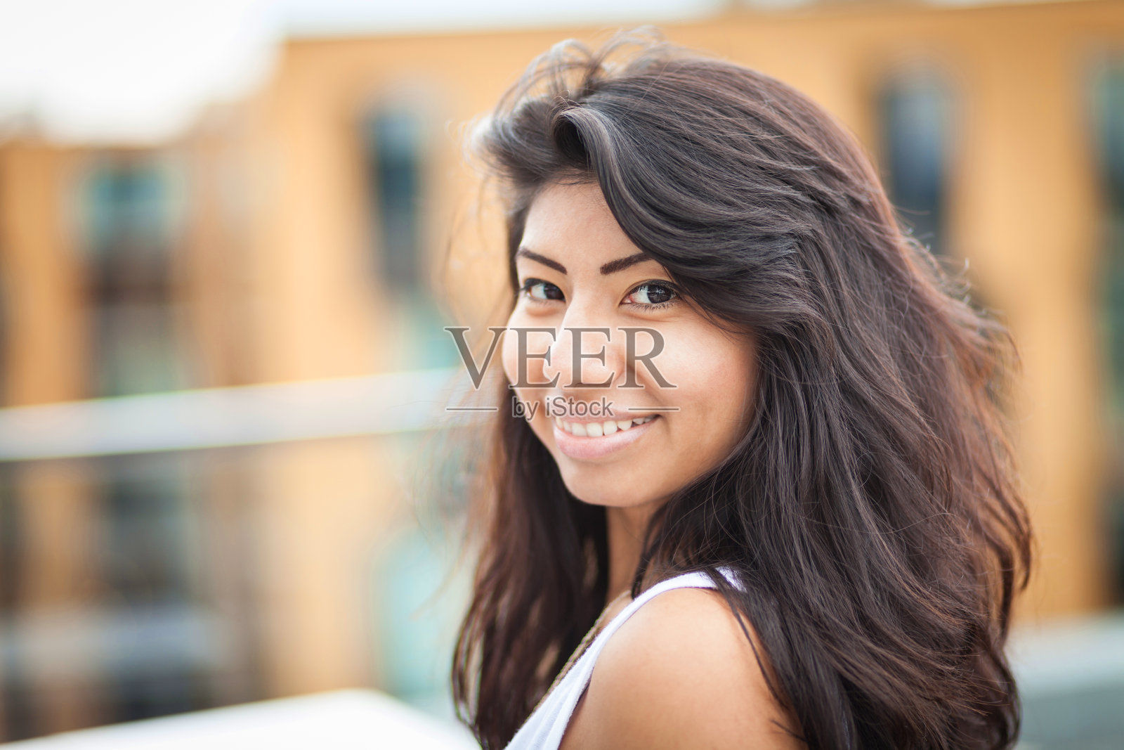 年轻的拉丁女人对着镜头微笑。她在外面的楼顶上照片摄影图片