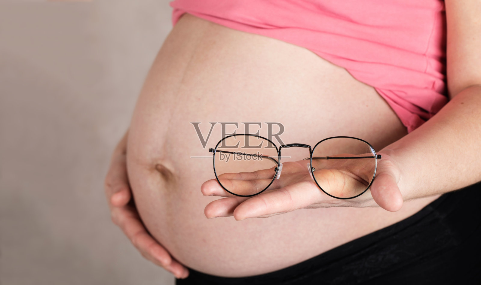 30到35岁之间的年轻孕妇把眼镜放在肚子前。照片摄影图片