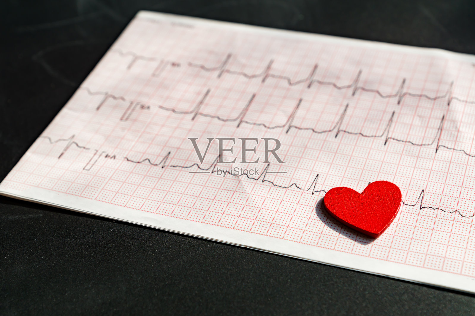 一个用红色木制心脏的纸形式的心电图的特写。黑色背景的心电图纸。医疗保健理念。照片摄影图片