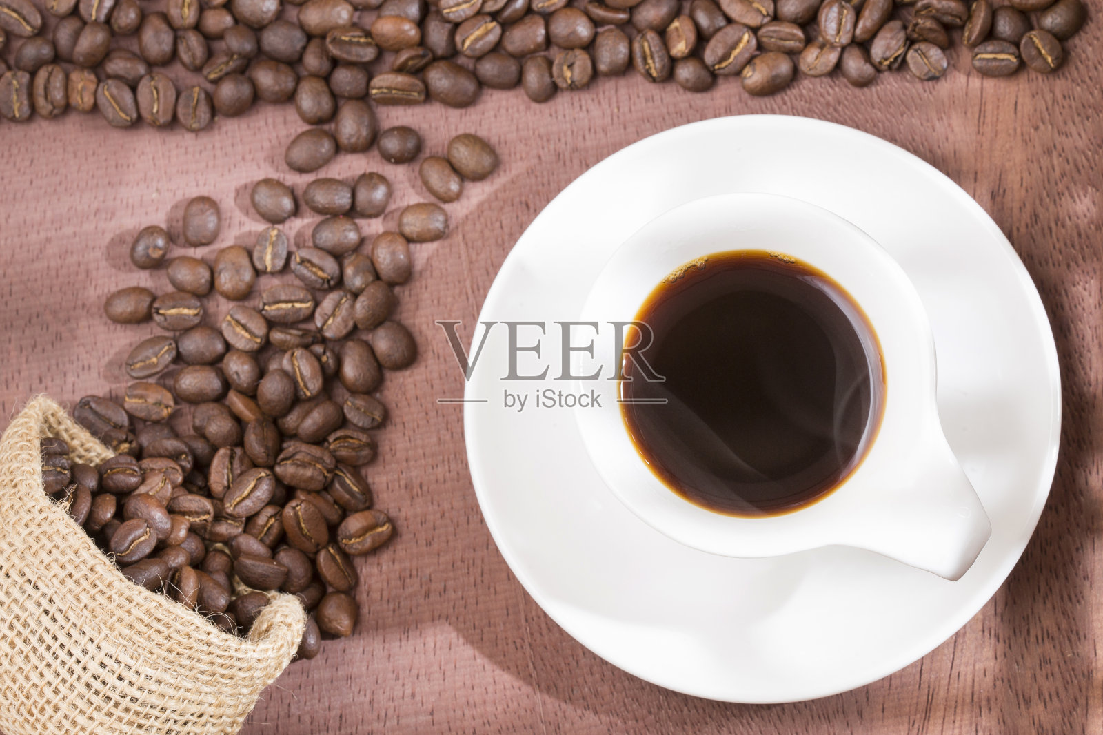 木桌上放着咖啡杯和咖啡豆，以麻袋为背景，复古色调照片摄影图片