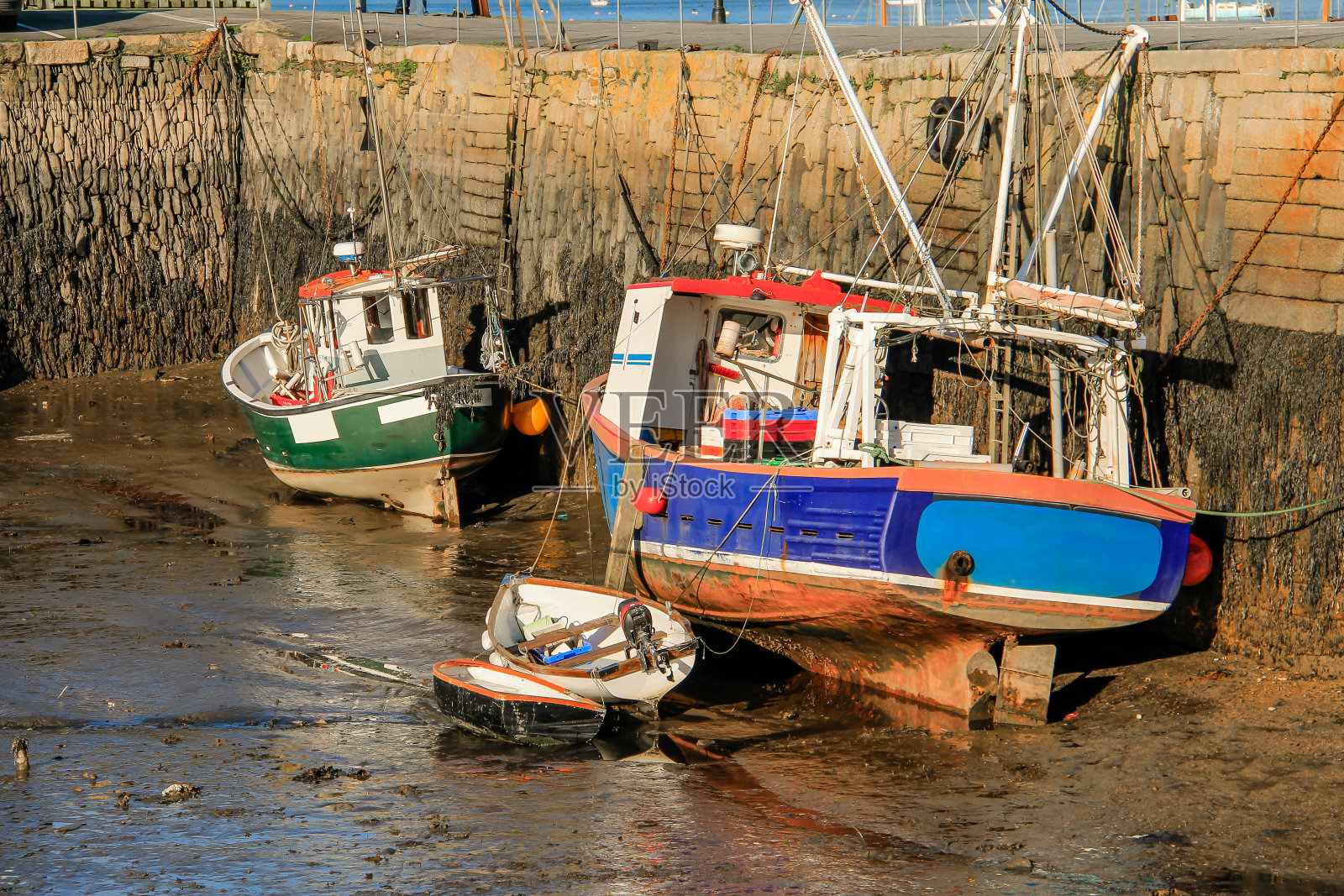 退潮时淤泥上的渔船，由康沃尔郡法尔茅斯的历史石港湾墙保护照片摄影图片
