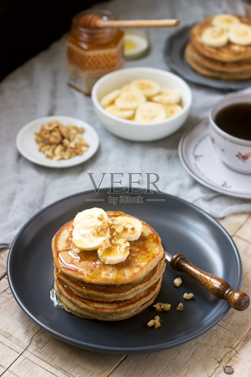 煎饼配香蕉、坚果和蜂蜜，配茶。乡村风格。照片摄影图片