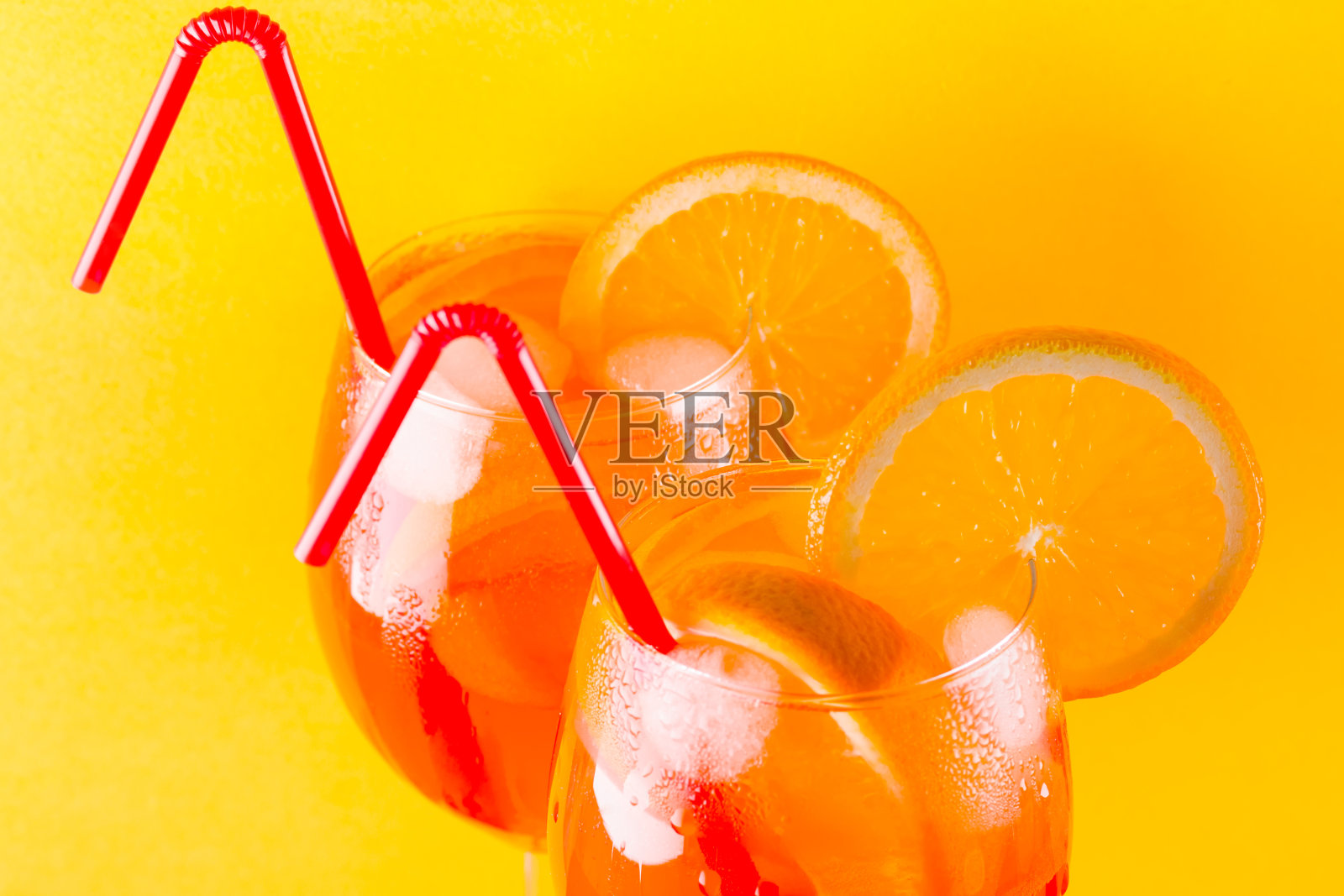 鸡尾酒喷在红黄背景上。夏日酒精鸡尾酒配橙子片。喷上彩色背景。极简主义风格的珊瑚色鸡尾酒照片摄影图片