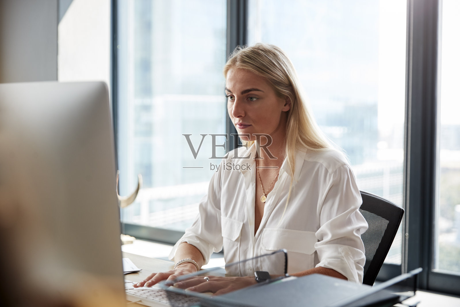 年轻的白色金发女子坐在办公桌前工作在一个创意办公室的电脑，近照片摄影图片