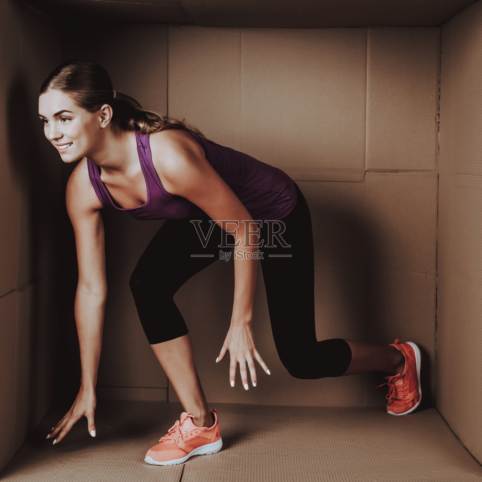 年轻女子在纸板箱里做运动。照片摄影图片