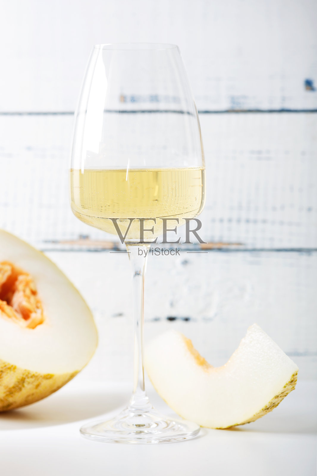 复古木桌上放着一杯白葡萄酒和一片新鲜甜瓜。光背景照片摄影图片