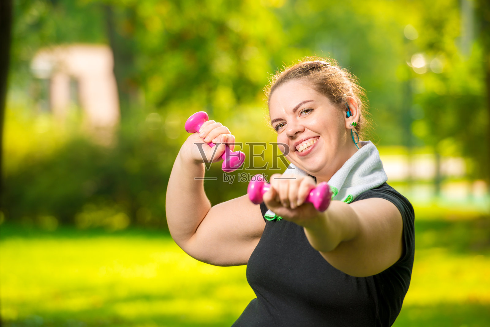 微笑的胖女人与哑铃在公园锻炼的肖像照片摄影图片
