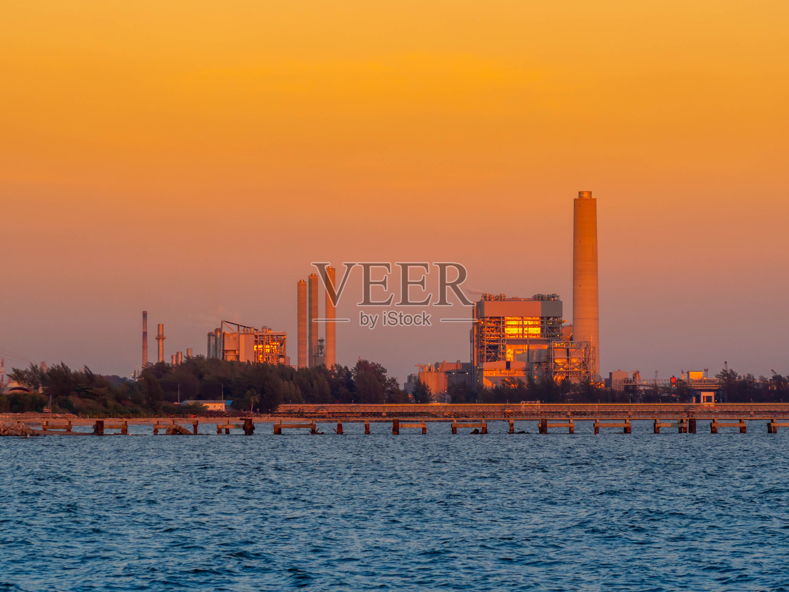 石油和天然气精炼工业工厂日落在海岸。照片摄影图片