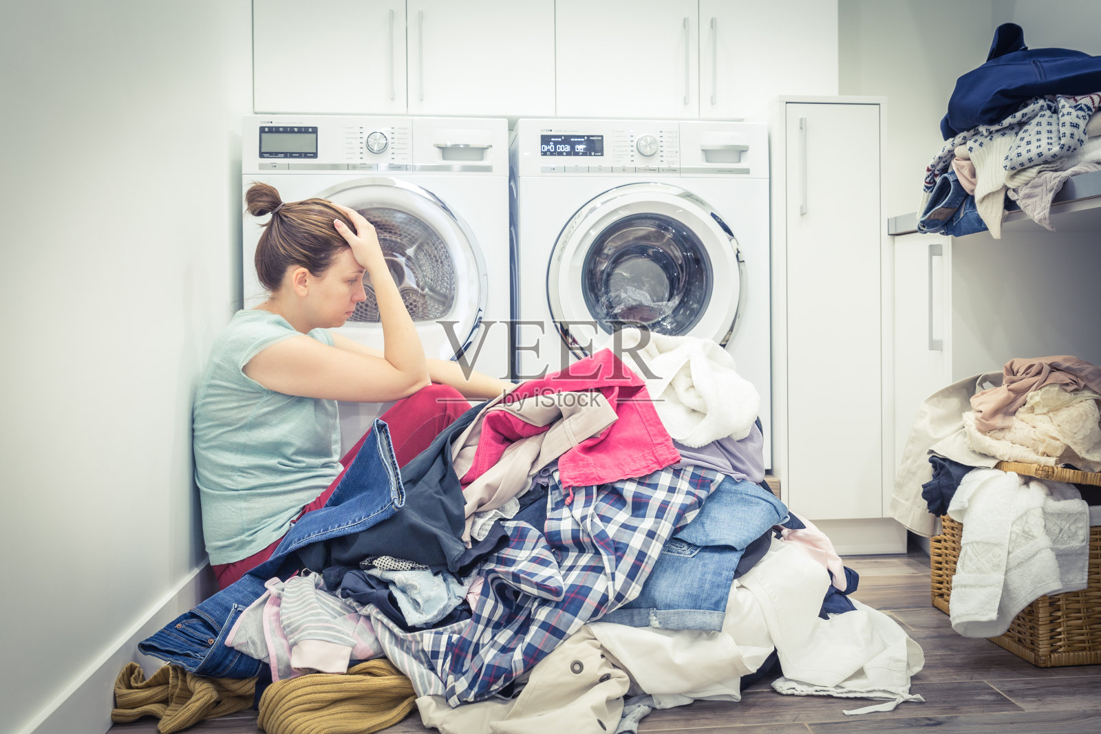 不快乐压力大的女人，在洗衣房的洗衣机旁边堆着一堆衣服，蓝色调照片摄影图片