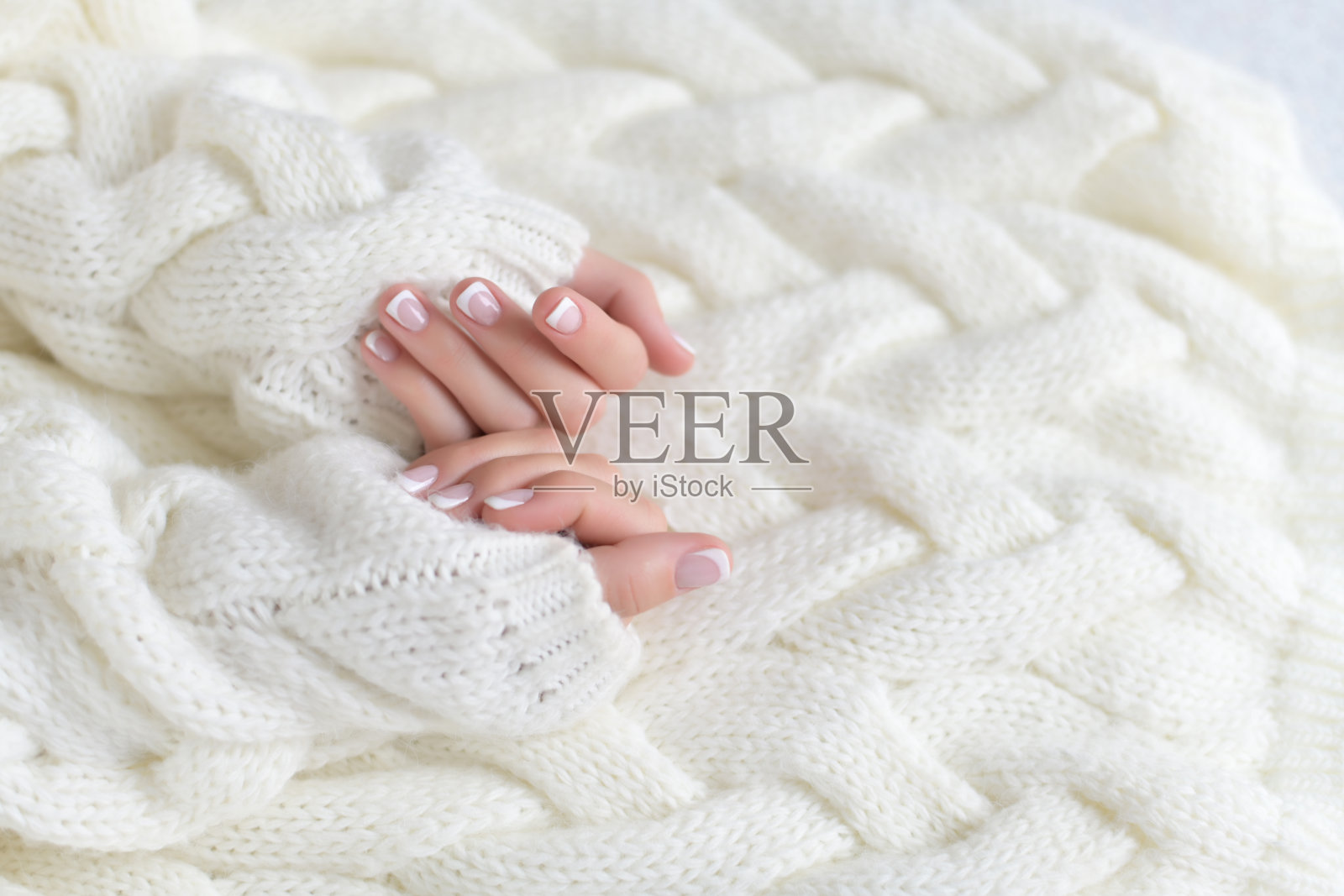 女人美丽的手与法式美甲的背景白色温暖的毛衣照片摄影图片