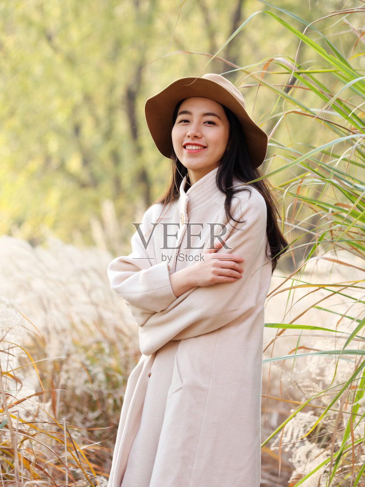 美丽的中国年轻女子在米色外套和帽子摆姿势和微笑的镜头，迷人的中国女孩与黑色的长发享受她的休闲户外时间。照片摄影图片