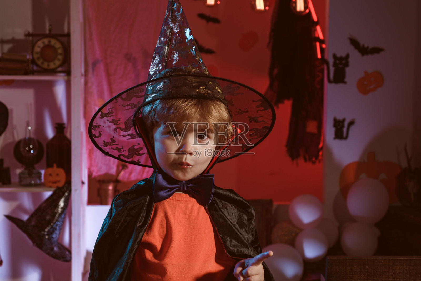 可爱的万圣节小巫师。神奇的帽子。孩子们玩南瓜并请客。魔术的秘密。节日的概念。万圣节快乐!照片摄影图片