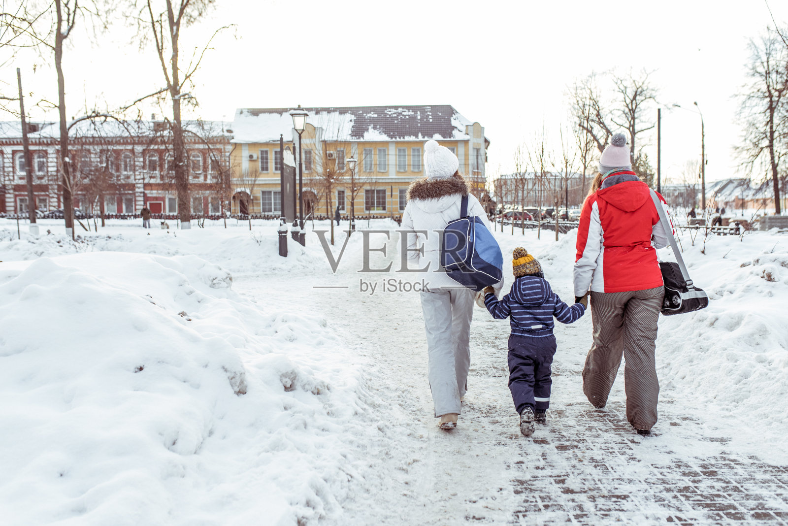 两个女孩女朋友女人在冬天带着一个3-5岁的小孩去，从后面看，雪堆雪景，雪道在城市里。自由空间。后视图。照片摄影图片