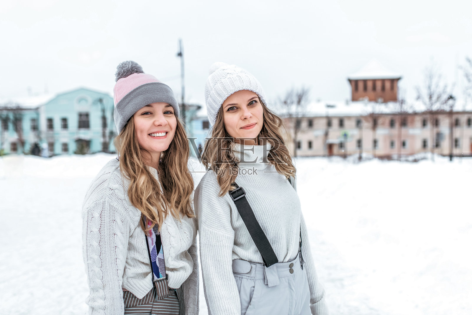 两个女孩的女朋友冬天骑滑冰场运动服暖和的衣服，毛衣连衣帽。快乐微笑有休息周末。城市溜冰场，雪堆雪背景。情感快乐快乐幸福。照片摄影图片