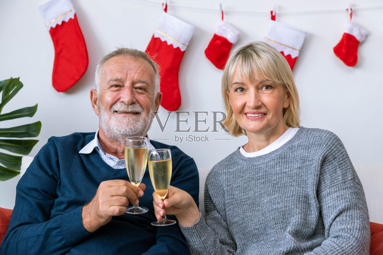 老两口男女拿着香槟聊天，坐在以圣诞树和装饰为背景的沙发上;看相机照片摄影图片