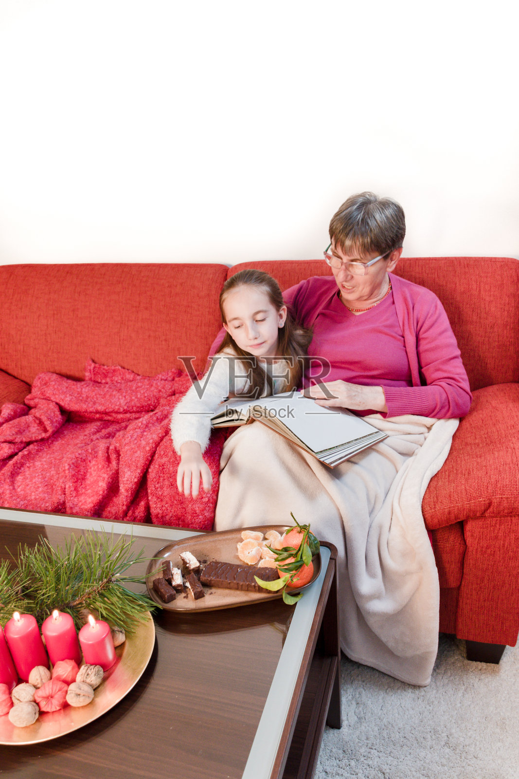 祖母和孙女在沙发上享用传统的圣诞牛轧糖(意大利Torrone)和橘子照片摄影图片