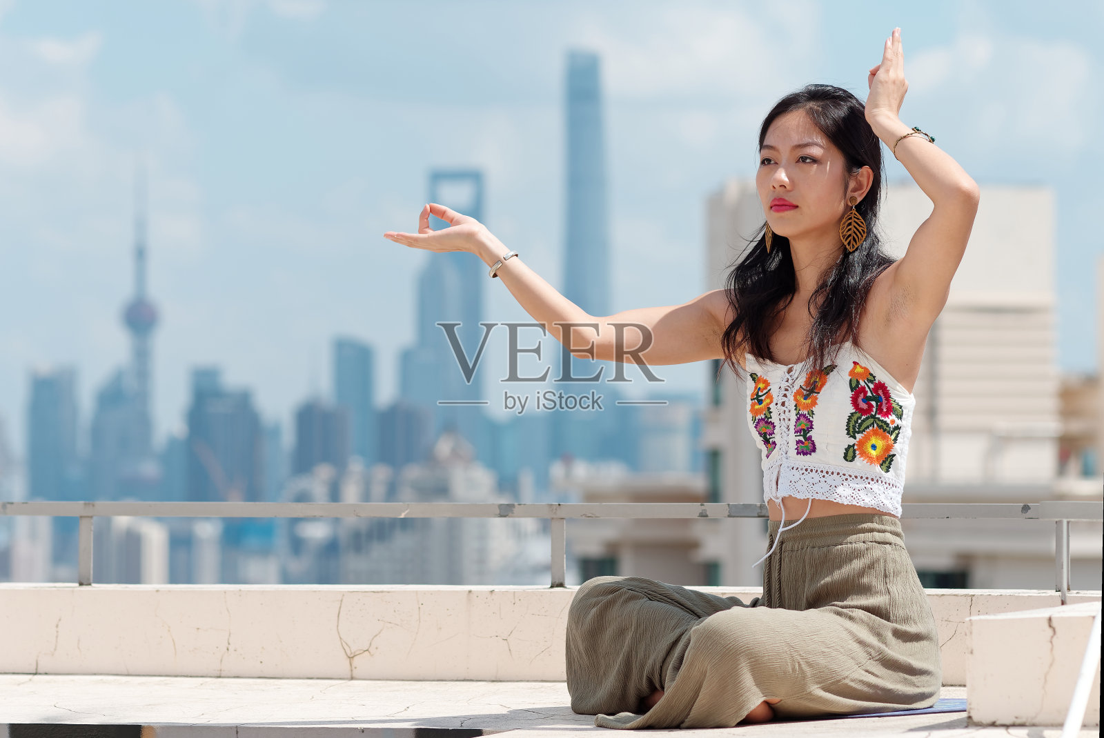 美丽的中国女人穿着运动服在以上海天际线为背景的建筑上练习瑜伽和冥想，年轻女性在阳光明媚的日子里做瑜伽体式。照片摄影图片