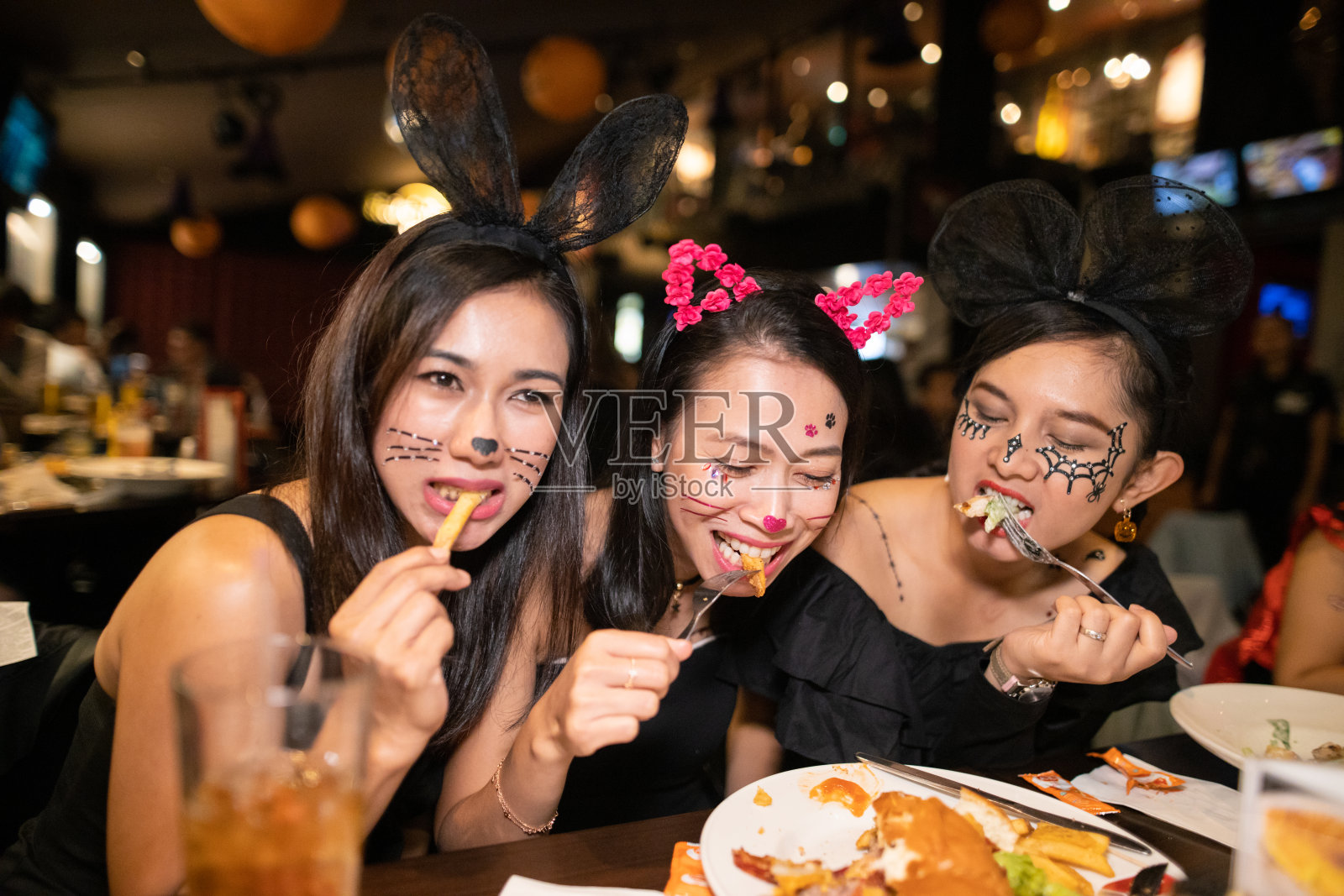 亚洲女人穿着万圣节服装一起在餐厅吃晚餐照片摄影图片