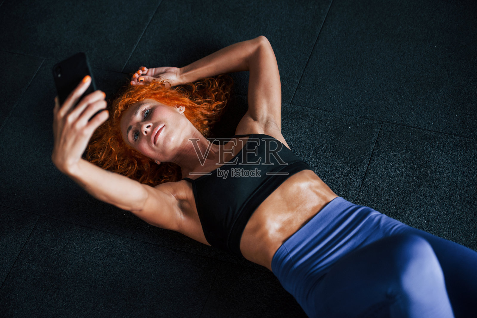 用手机自拍。喜欢运动的红发女孩白天去健身房健身。肌肉发达的身体类型照片摄影图片