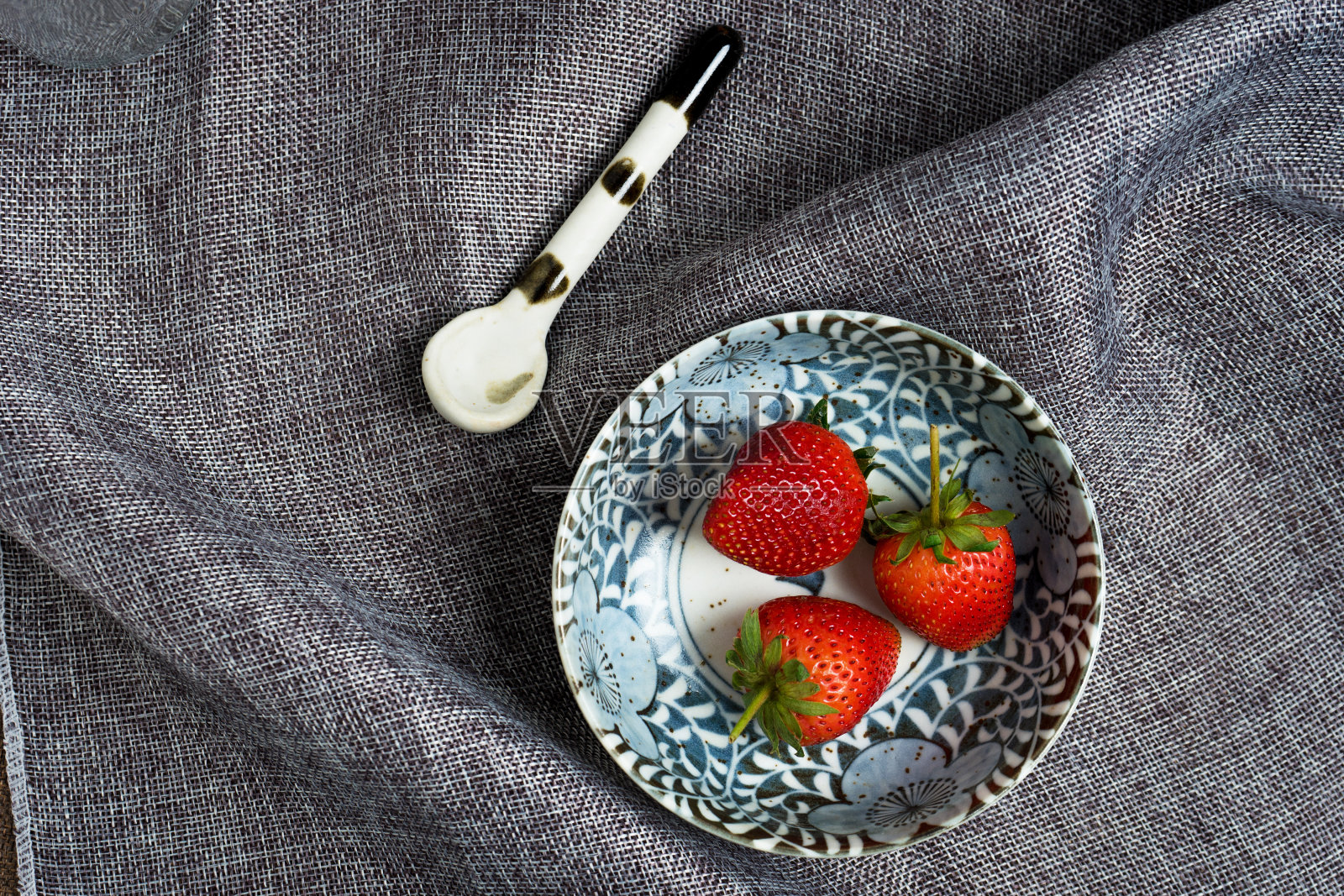 鲜草莓放在瓷碗里，灰碟布上照片摄影图片