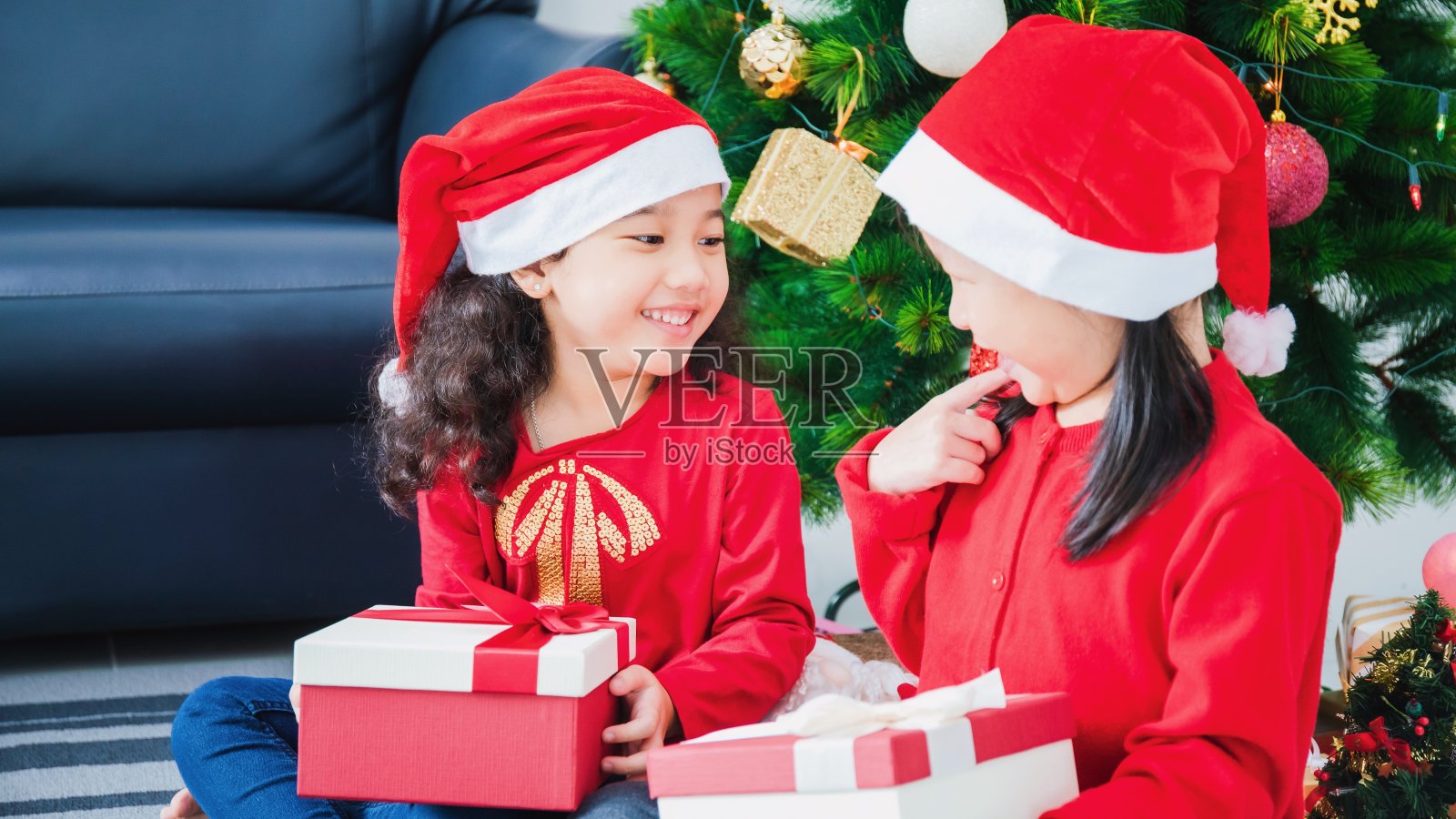 亚洲小女孩和朋友一起在家里白色的房间里用礼盒装饰圣诞树。笑脸盈盈，与家人欢度新春佳节。照片摄影图片