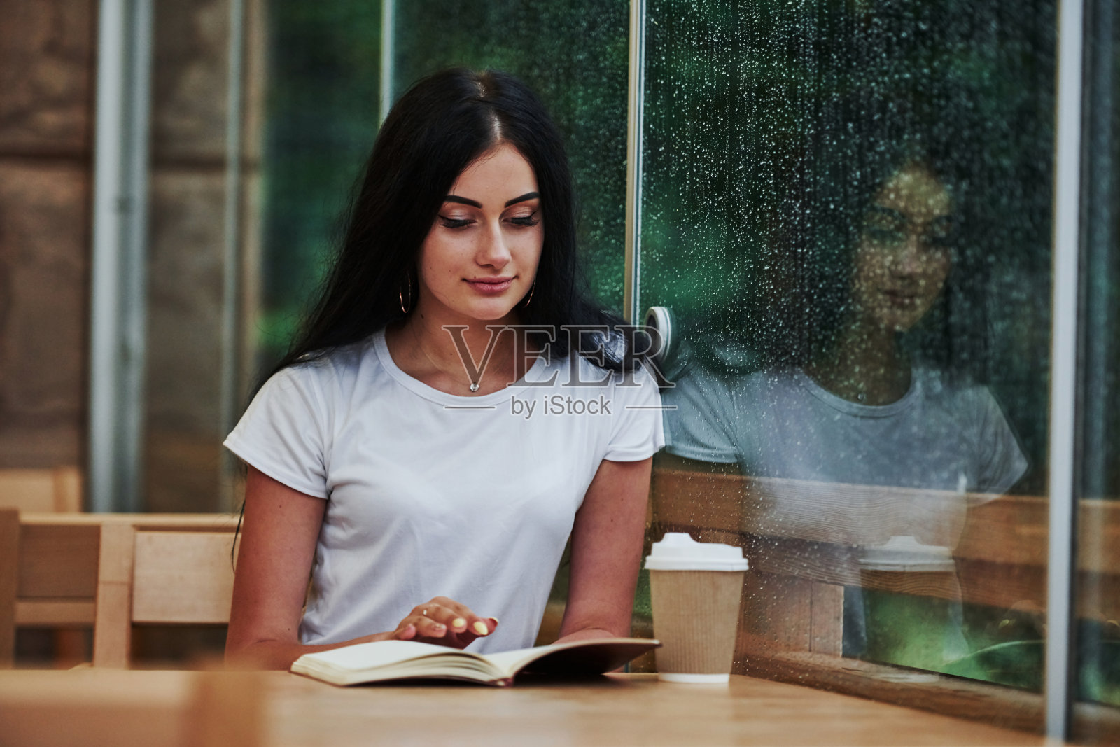 下雨天坐在咖啡馆里的年轻女学生的肖像。一个人只有照片摄影图片