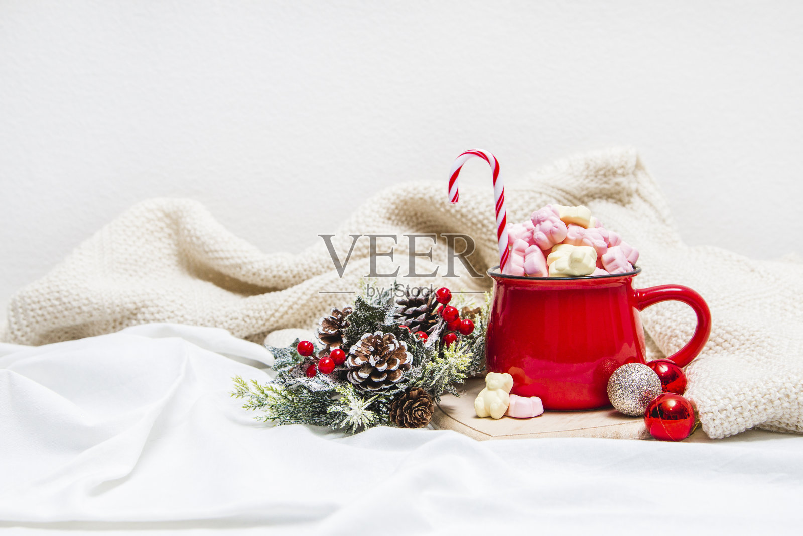 白色床单上放着棉花糖和冬季装饰品的红色杯子照片摄影图片
