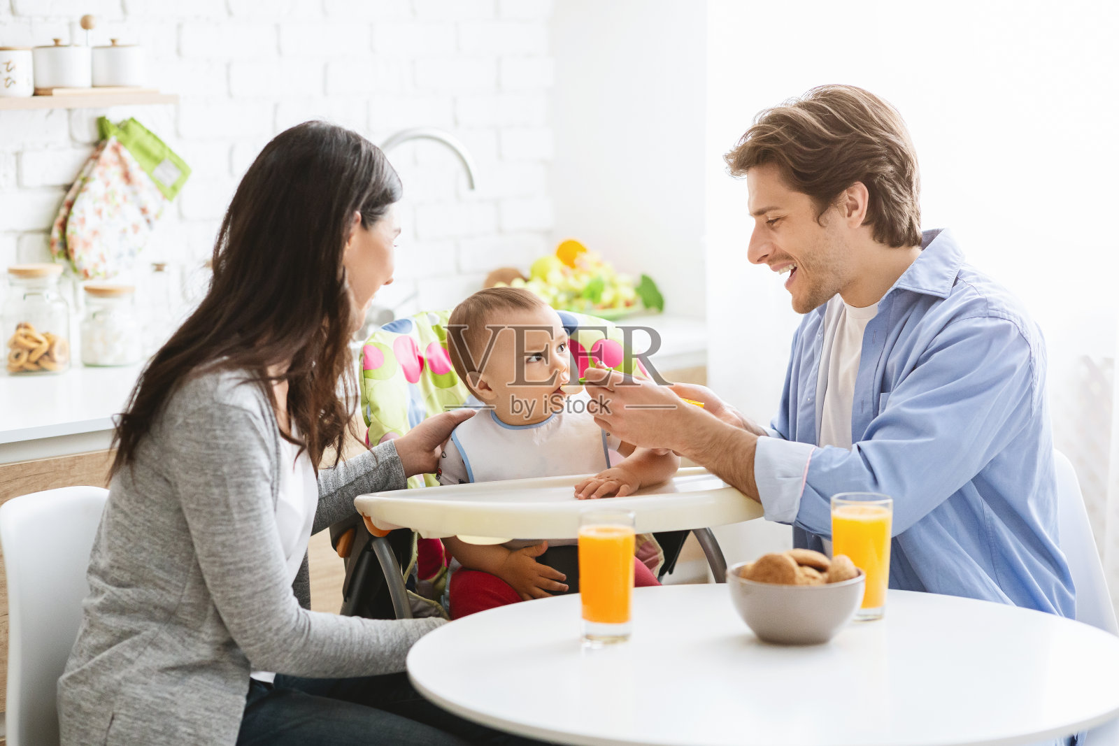 快乐的千禧一代父母在厨房给男婴喂食照片摄影图片