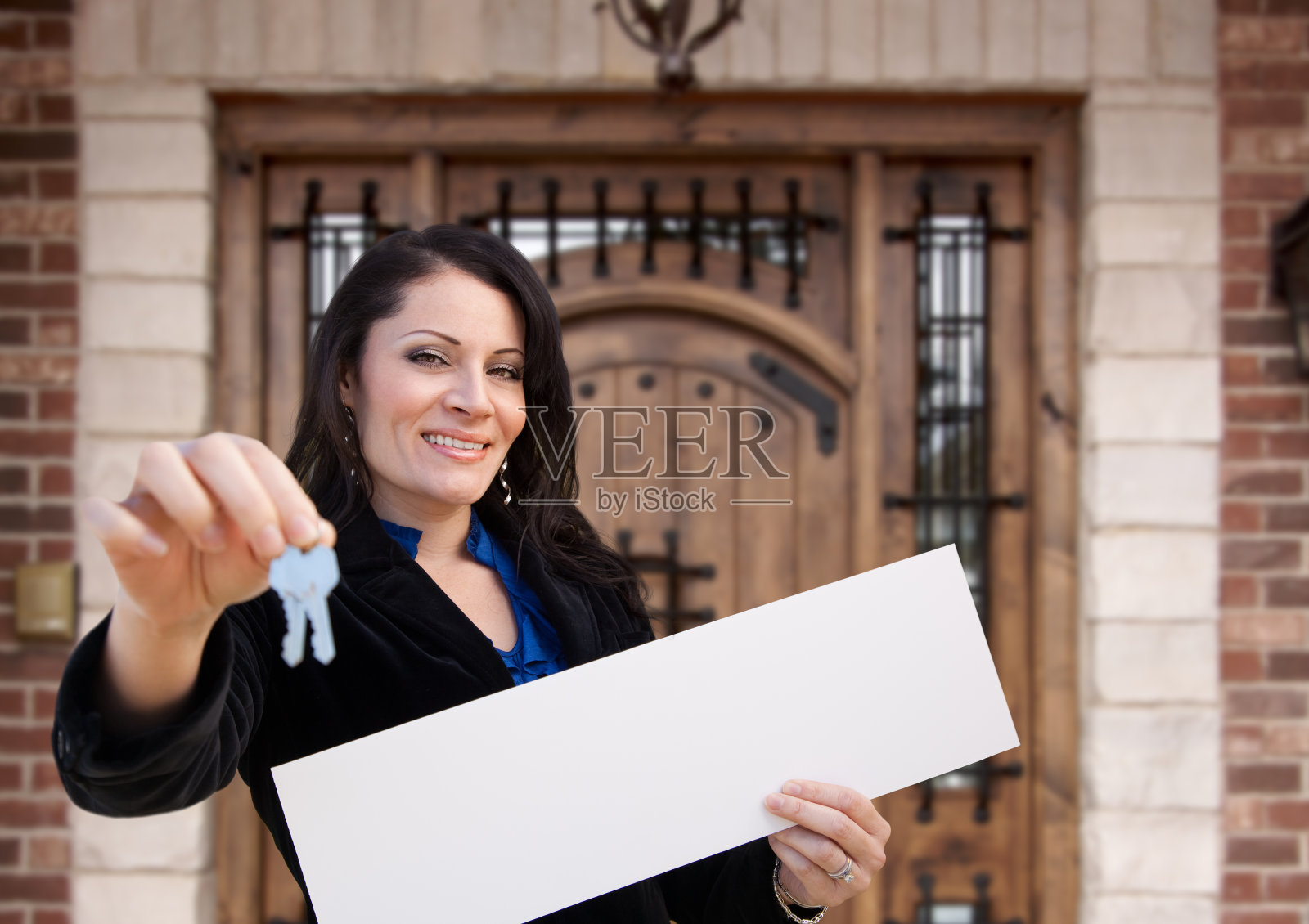 西班牙裔妇女拿着空白标志和钥匙在房子前面照片摄影图片