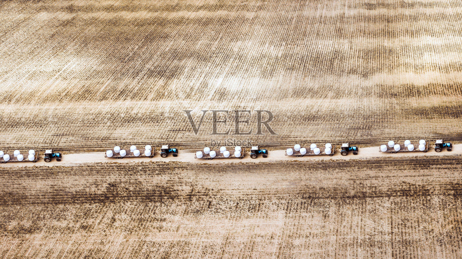 从田野鸟瞰图上看，一列拖拉机牵引着稻草照片摄影图片