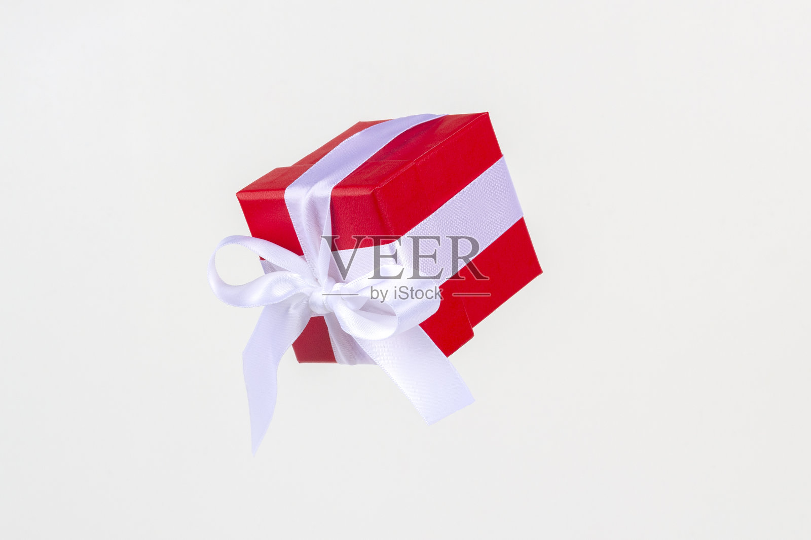 红色礼盒与白色缎带蝴蝶结飞舞在白色背景。最小的概念为圣诞节假期，生日，情人节，购物和销售。照片摄影图片