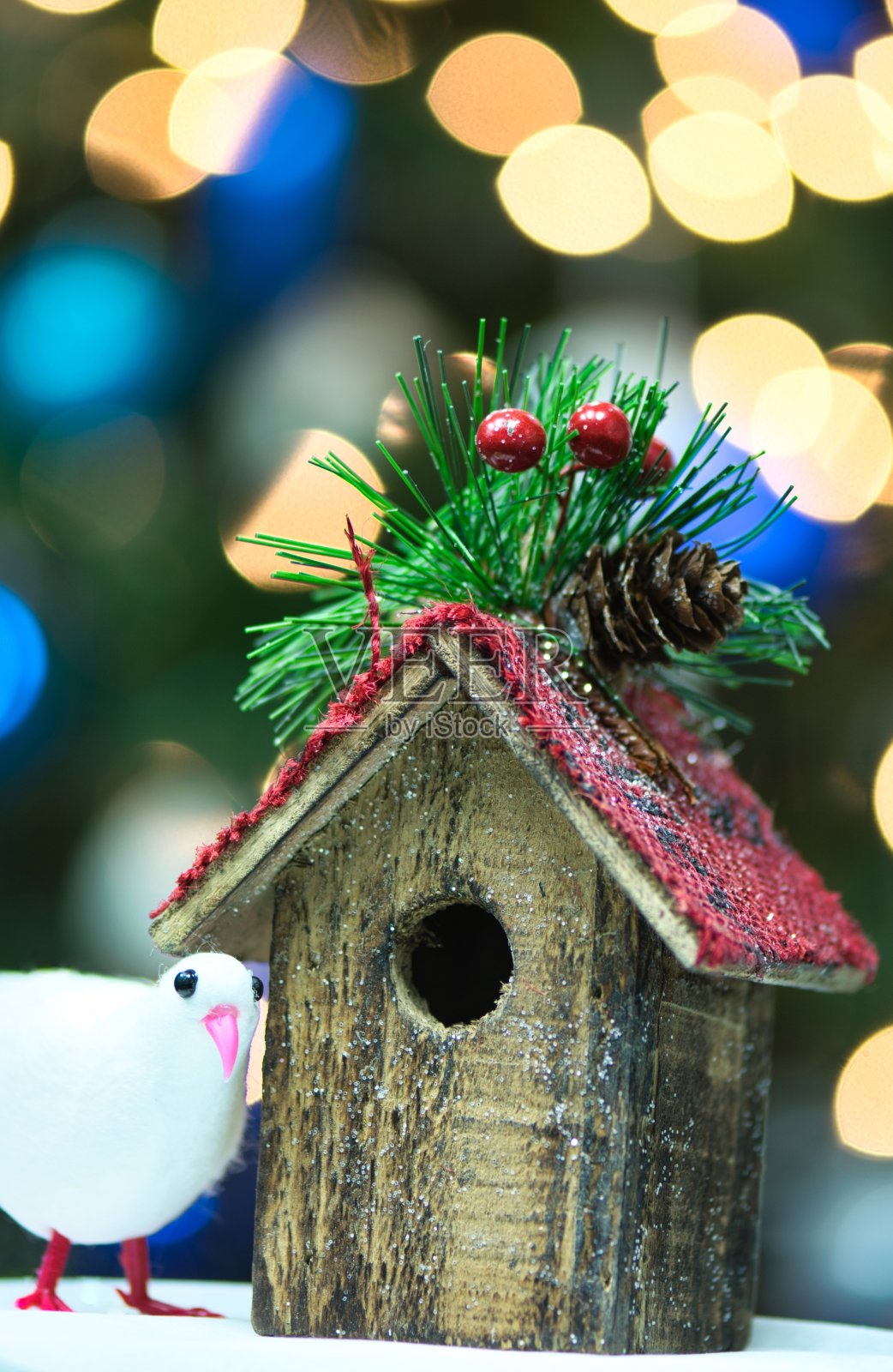 玩具鸟和挂着圣诞树灯的鸟屋。照片摄影图片