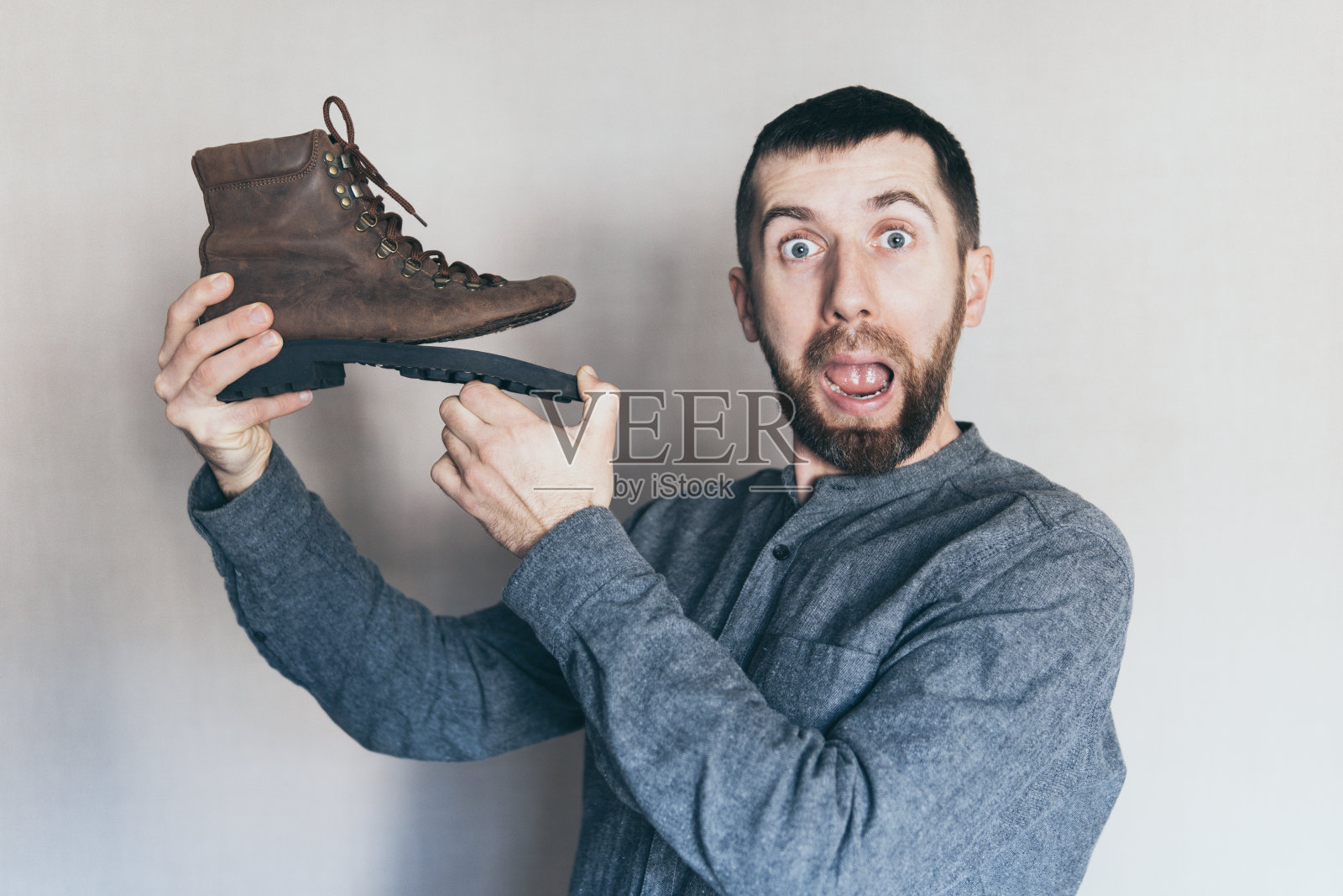 一个人拿着一只鞋底破了的旧皮靴，脸上露出惊讶和震惊的表情照片摄影图片