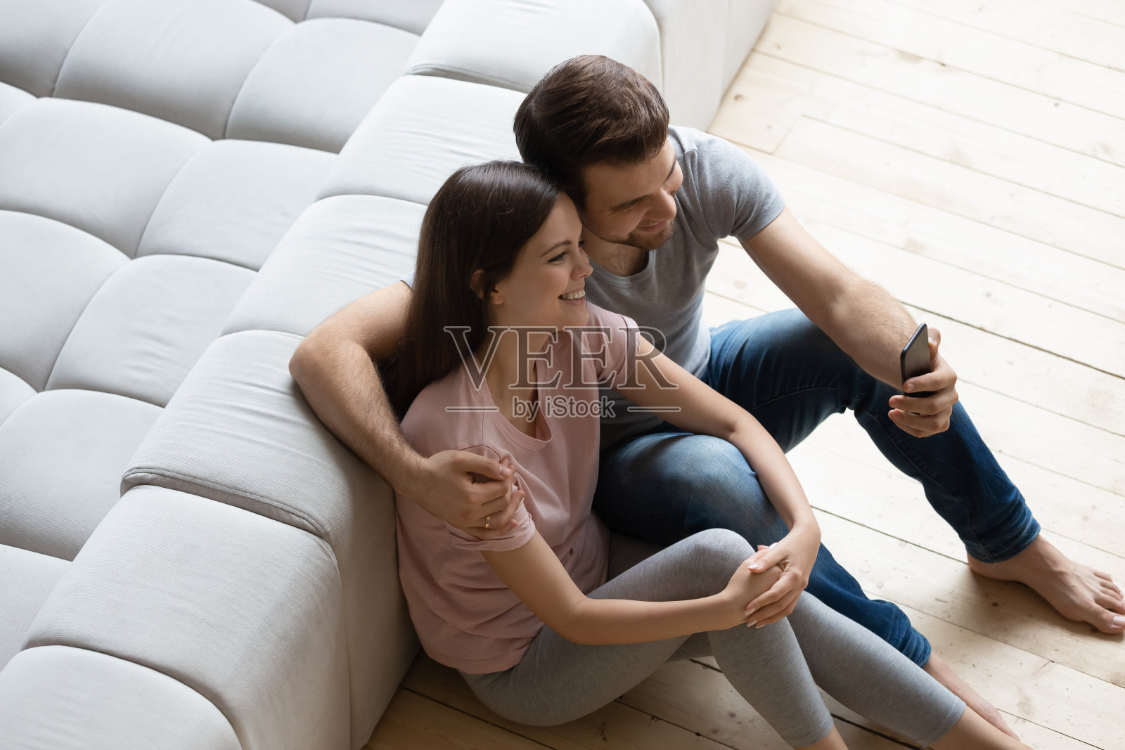 一对夫妇坐在温暖的木地板上，拿着智能手机自拍照片摄影图片