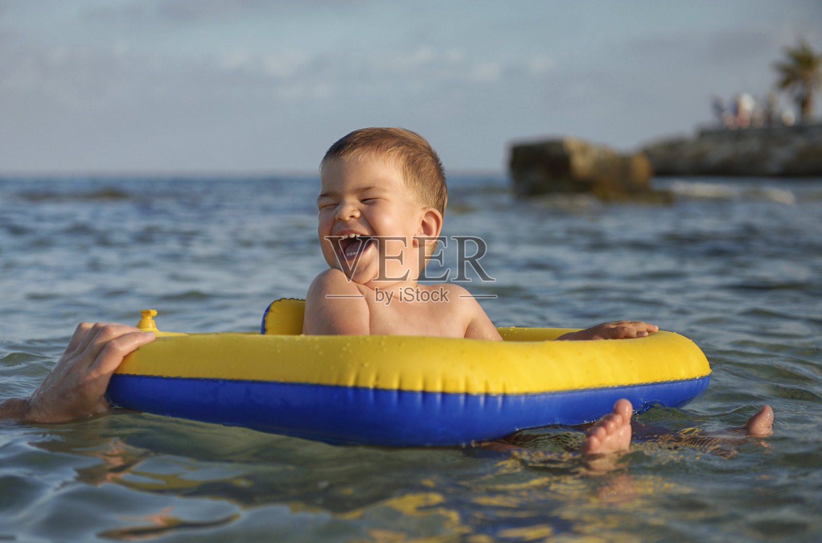 小男孩在蹦蹦跳跳的黄色圆圈里在海里游泳照片摄影图片