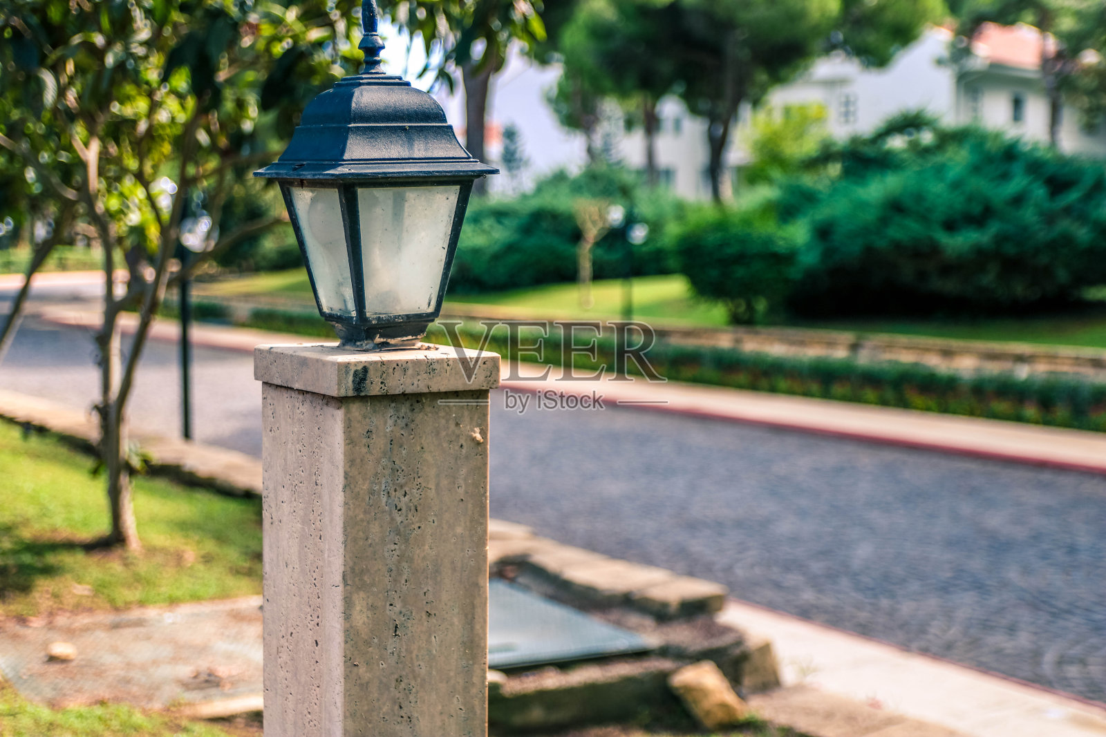 一种街道花园地灯，安装在一个公园的绿色草坪上，靠近一个在夏季花园散步的石头小径。照片摄影图片