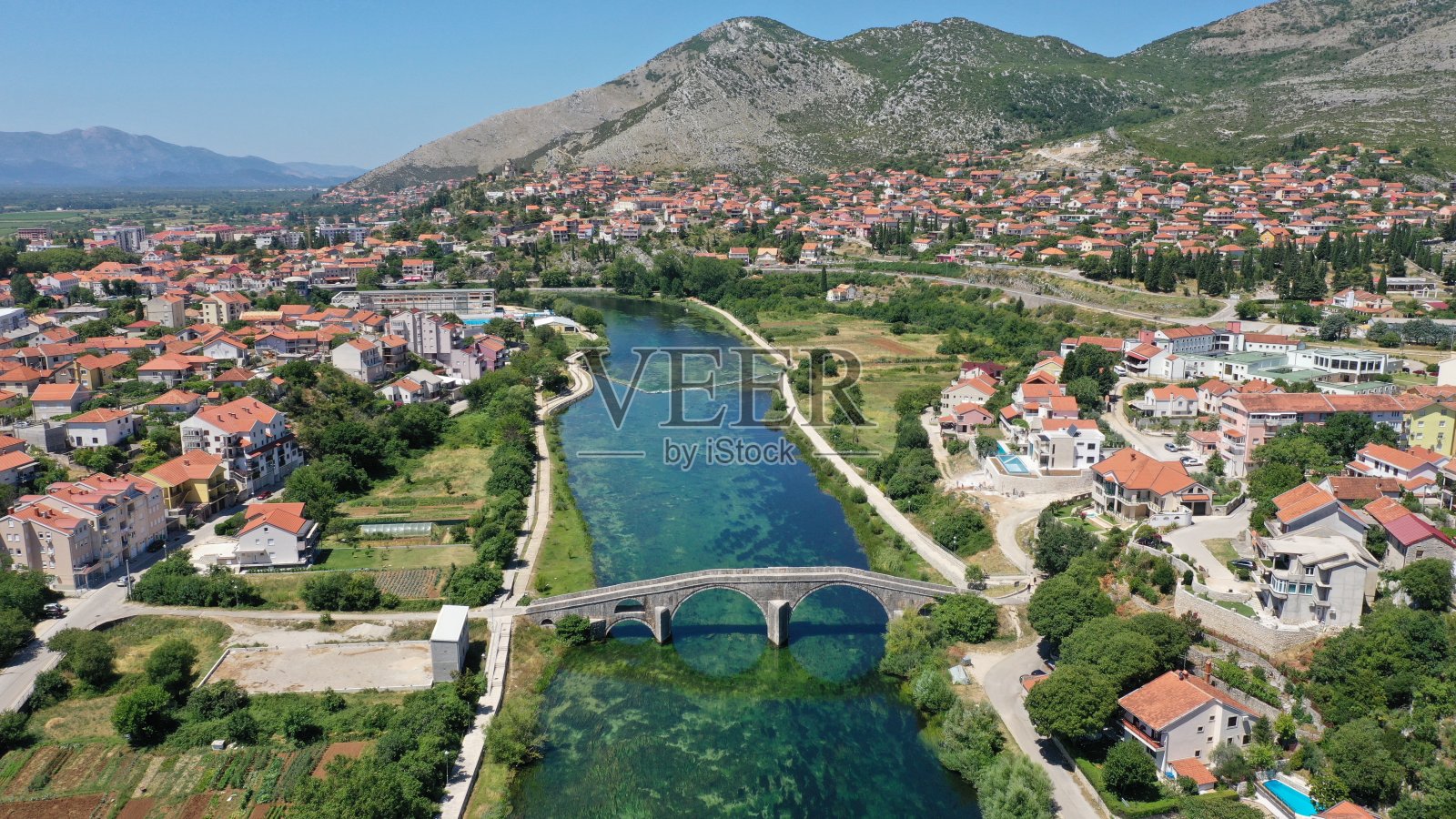 特雷宾耶老城特雷比斯吉卡河上阿斯拉尼奇大桥的鸟瞰图。波斯尼亚和黑塞哥维那。夏日阳光明媚，绿油油的水、山、树、蓝天、小房子。照片摄影图片
