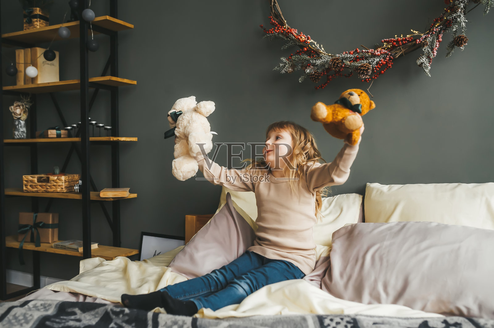 漂亮的小女孩坐在圣诞树旁的床上玩玩具熊。照片摄影图片