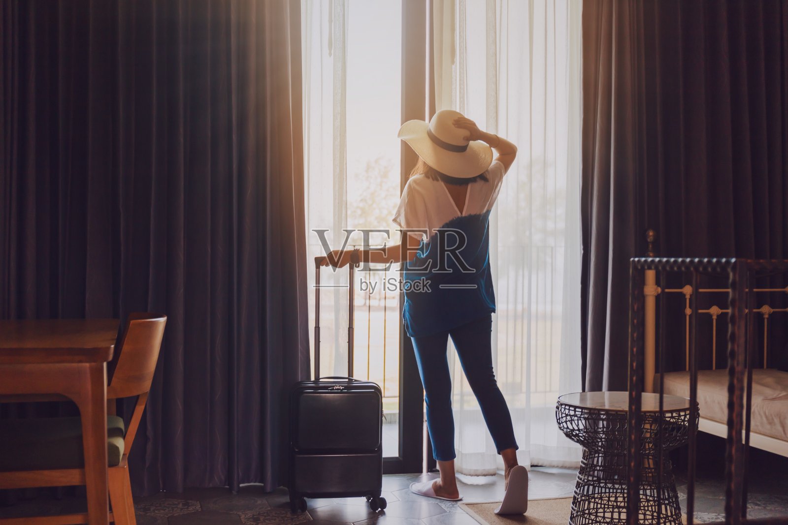 亚洲女性拿着行李住在酒店房间里。打开房间的窗帘和门，看看外面的景色。假日旅游概念。复古的基调。照片摄影图片