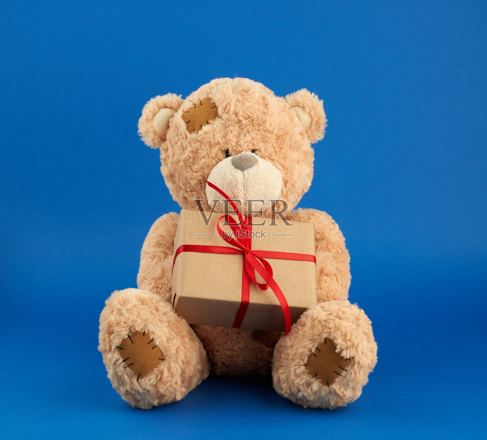 米黄色的大泰迪熊拿着一个用棕色纸包着的盒子照片摄影图片