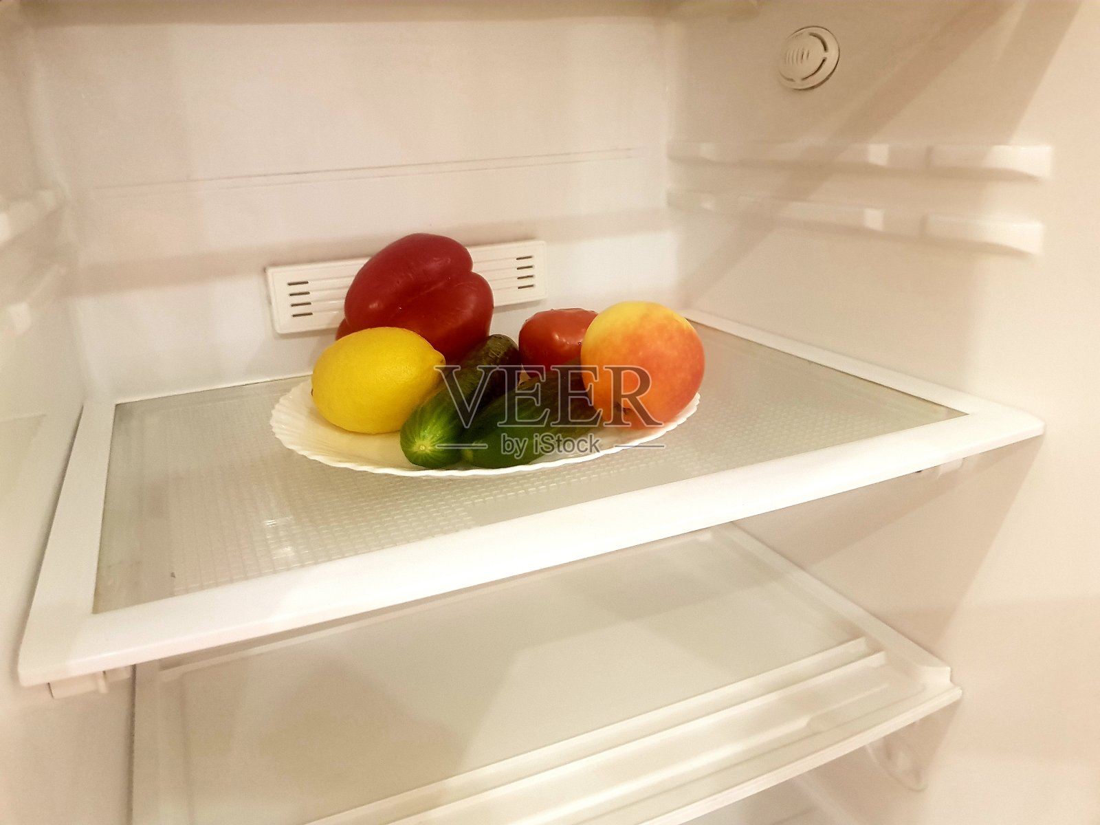 装着蔬菜和水果的盘子放在空冰箱的架子上。有机产品的可持续消费理念照片摄影图片