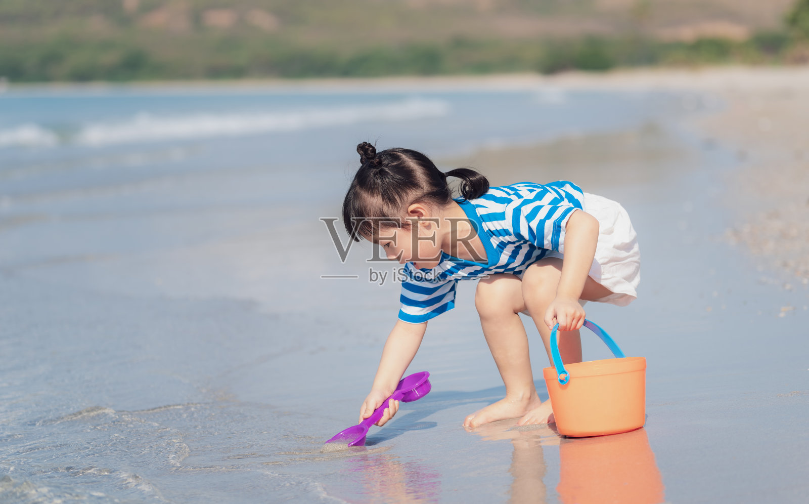 亚洲小女孩在沙滩上玩沙子。三岁的孩子玩沙玩具。幸福的家庭的概念照片摄影图片