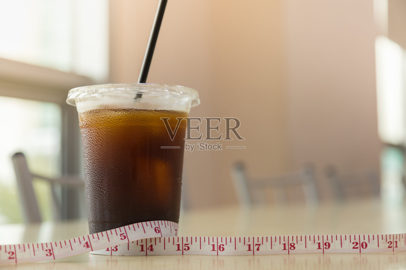 饮食和食物概念。关门的外卖塑料杯冰黑咖啡(美式咖啡)与测量磁带在桌子上的餐厅商店与复印空间。照片摄影图片