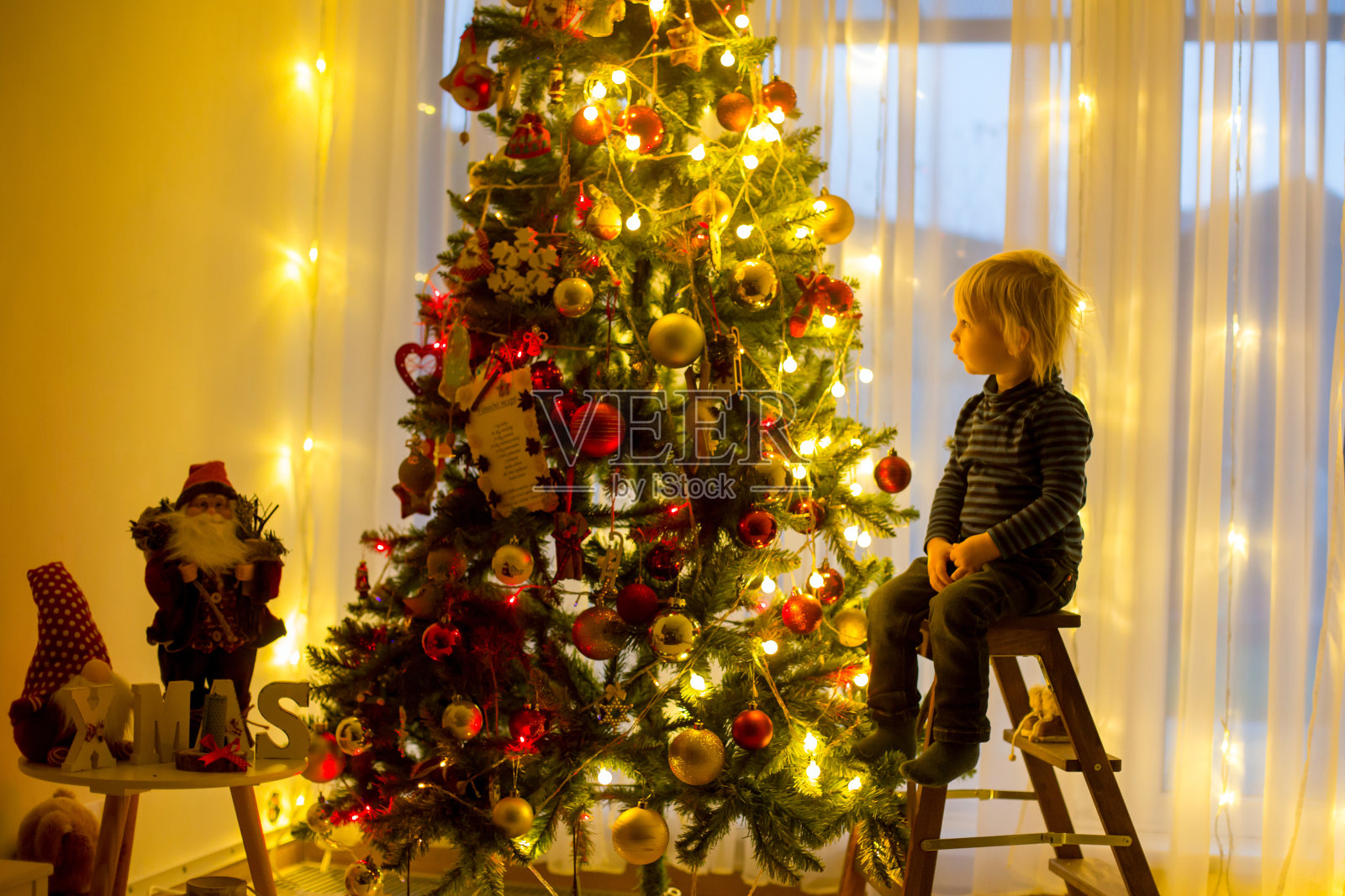 漂亮的金发小孩，用球和灯绳装饰圣诞树照片摄影图片