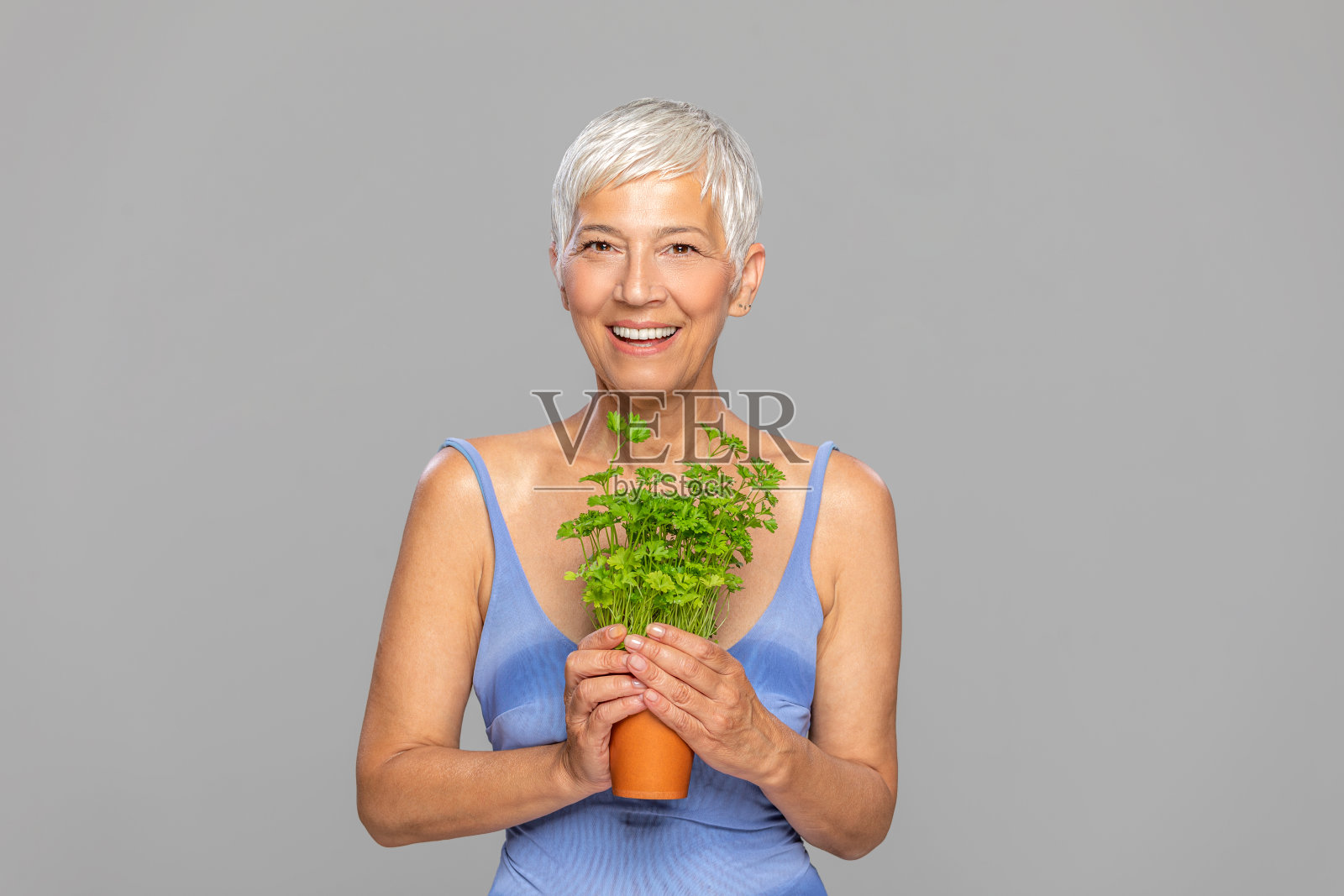 快乐的妇女与绿色植物在橙色的花盆在灰色的背景。照片摄影图片