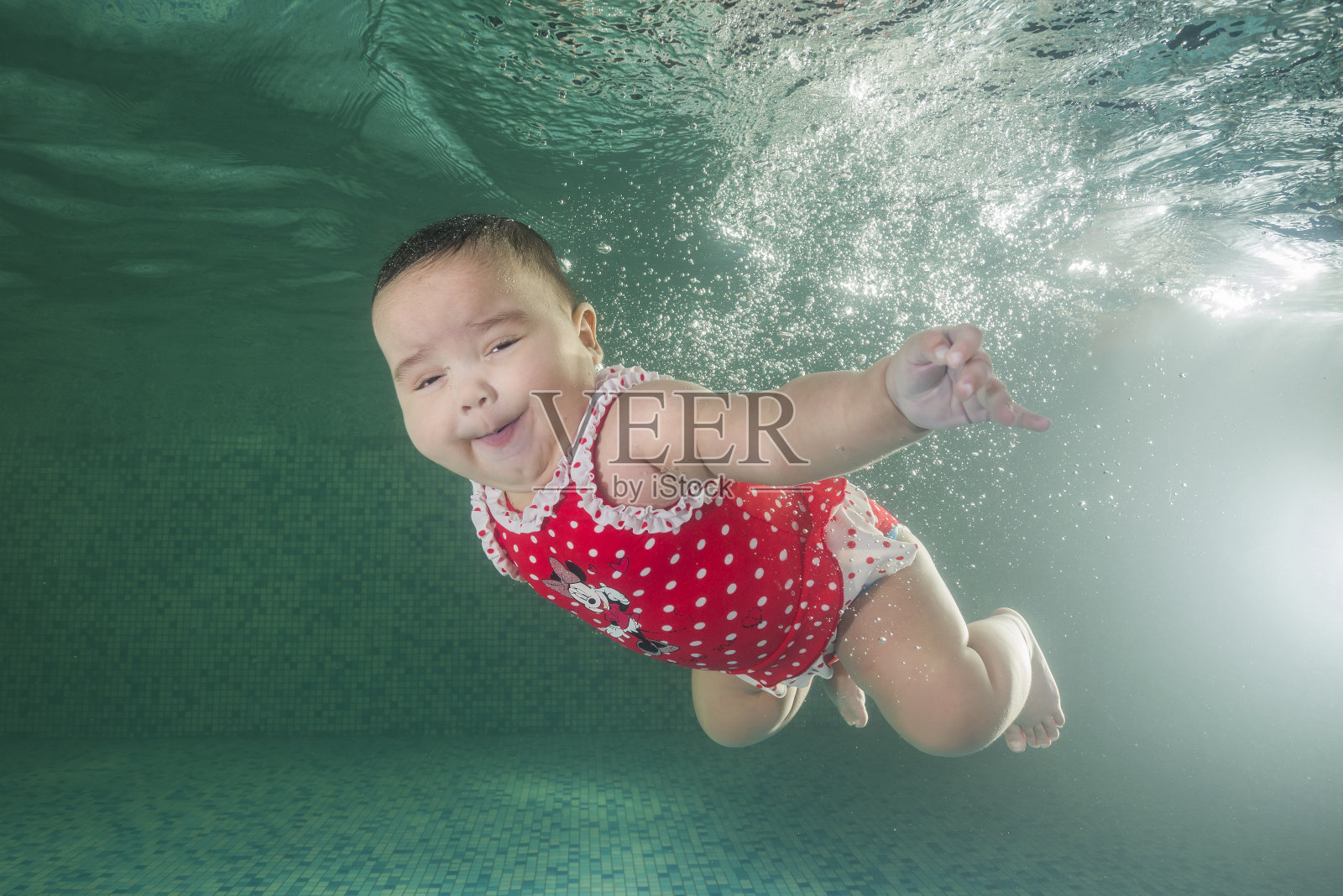 一个穿着红色游泳衣的小女孩在游泳池里学习游泳。婴儿在游泳池里游泳。健康的家庭生活方式和儿童水上运动。儿童发育，疾病预防照片摄影图片