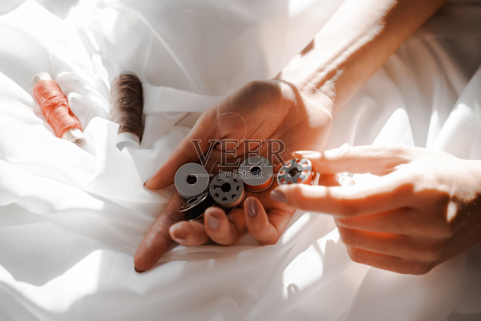 女性的手在白色织物的背景下，手中拿着机器切割的线轴。缝纫，设计工作，裁缝工作室，裁缝，设计师服装，制造厂照片摄影图片