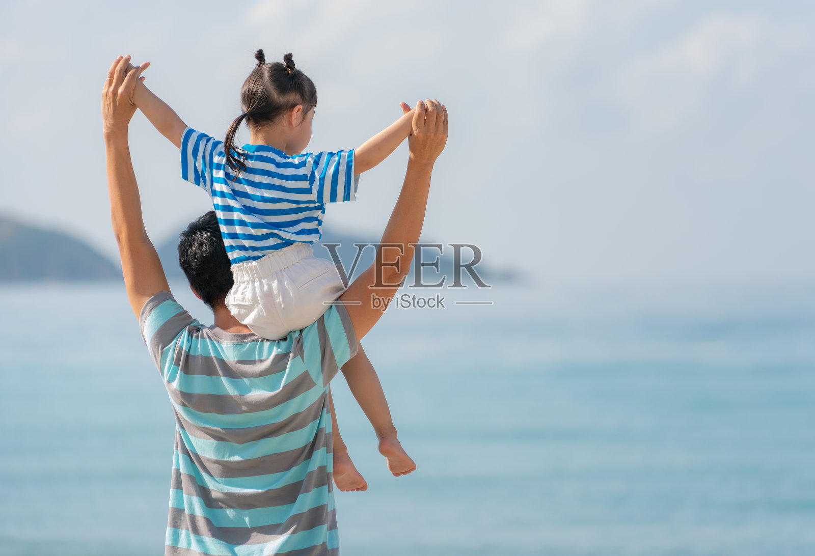 亚洲父亲和女儿在沙滩上，亚洲父亲把女儿抱在背上，同时举起左手。幸福的家庭的概念照片摄影图片